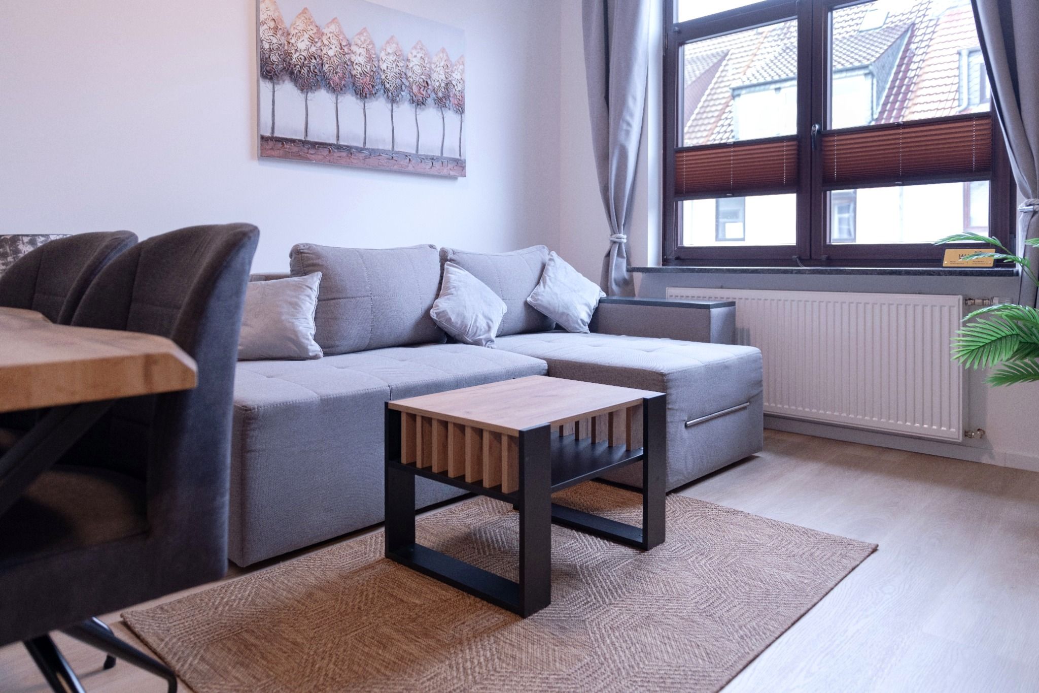 Ein modernes Wohnzimmer mit einem grauen Sofa, einem Holztisch und einem Bild an der Wand.