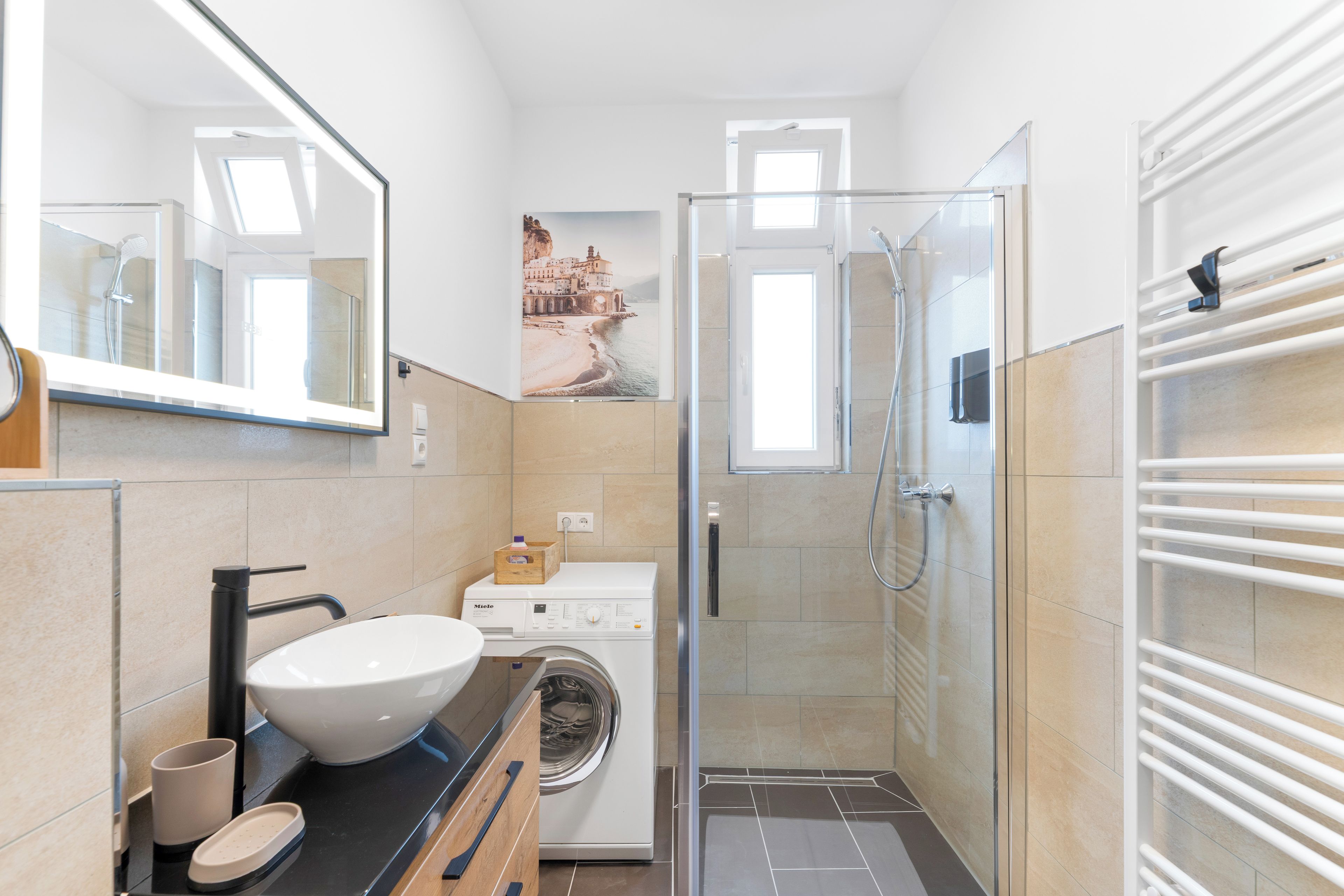 Ein kleines Badezimmer mit Waschbecken, Spiegel, Dusche und Waschmaschine.
