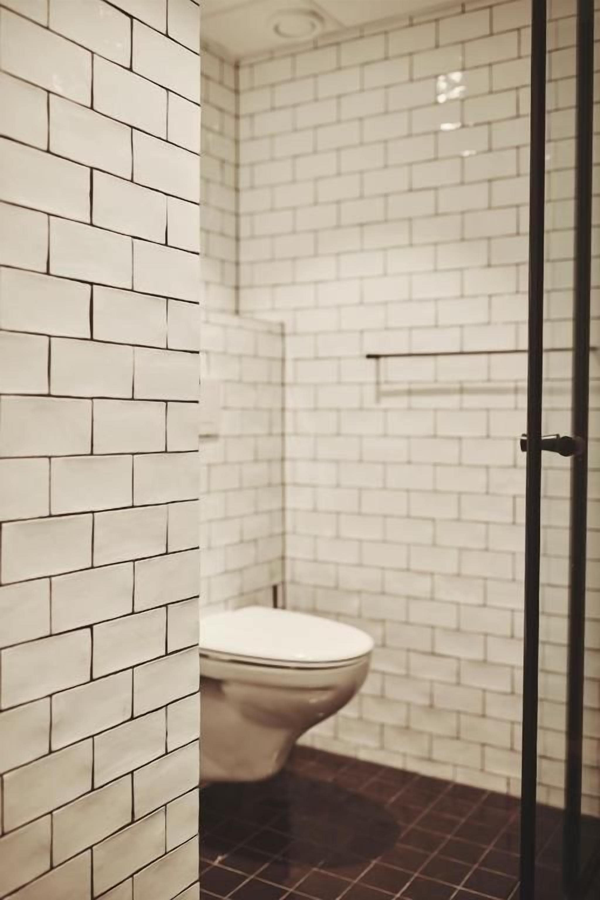 Un baño con azulejos blancos tipo metro, inodoro y cabina de ducha de vidrio.