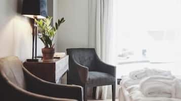 A hotel room with a bed, a chair, a desk with a lamp, and a window with curtains.