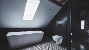 A modern bathroom with a freestanding bathtub, a toilet, and a skylight.