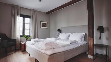 Una camera da letto con un letto, una sedia, un comodino, una lampada e una finestra con tende.
