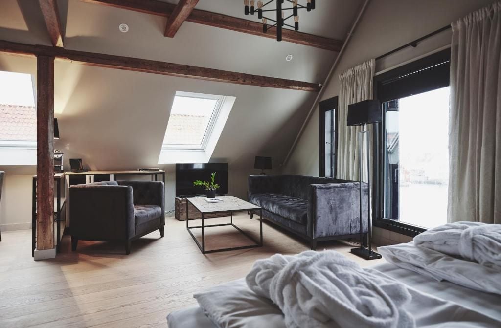 A loft-style bedroom with a sloped ceiling, a large skylight, a bed with white bedding, a dark sofa, a coffee table, and a TV.