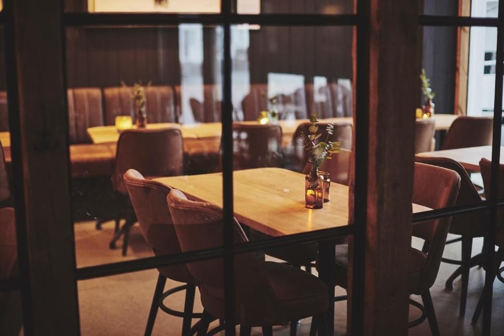 A restaurant interior with wooden tables and chairs, a glass partition, and a view of the street outside.