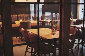 L’intérieur d’un restaurant, avec des tables et des chaises en bois, une cloison en verre et une vue sur la rue.