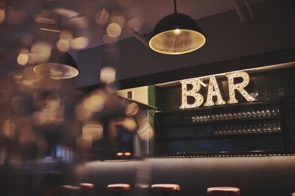Eine Bar mit einer Beschilderung mit dem Schriftzug 'BAR' und einer Reihe von Gläsern in Regalen.