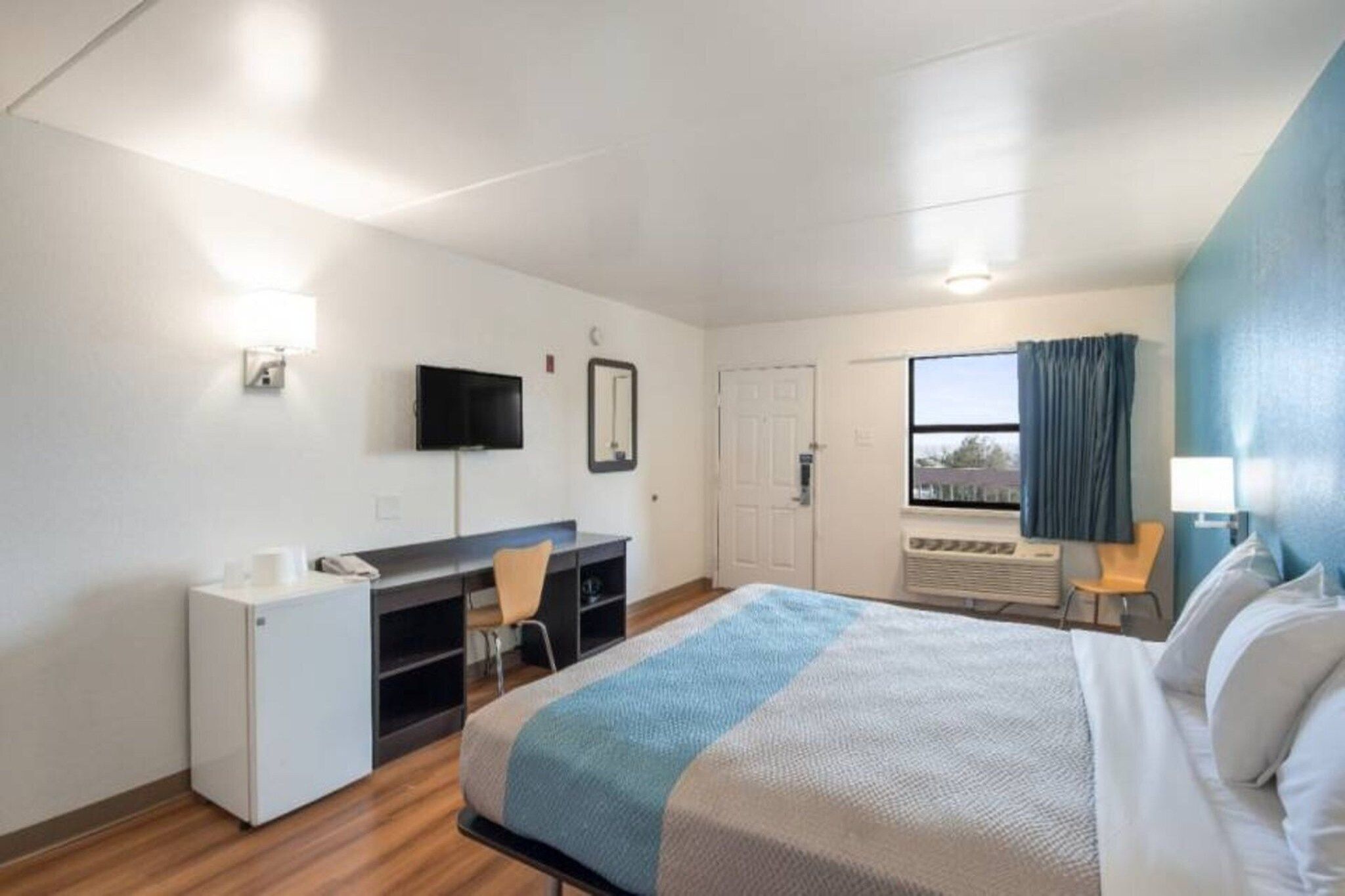 Une chambre d’hôtel équipée d’un lit, d’un bureau, d’une chaise, d’une télévision et d’une fenêtre avec des rideaux.
