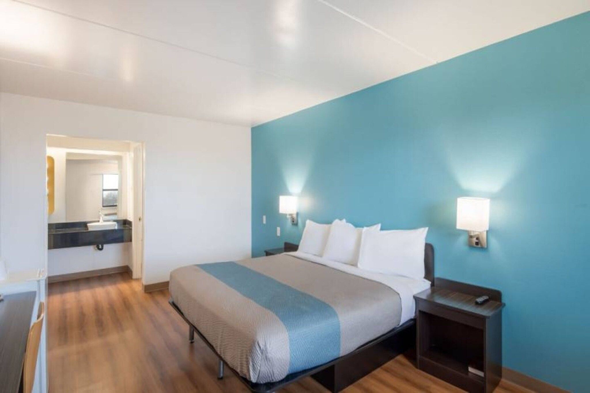 A hotel room with a bed, bedside tables, a nightstand, a mirror, and a bathroom with a sink and mirror.
