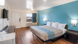 Habitación de hotel con cama, escritorio, silla, ventana con cortinas y televisor montado en la pared.