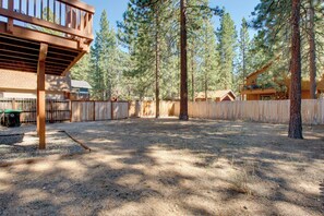 A fenced backyard with a wooden deck, surrounded by tall pine trees. - Walk to Lake! Spacious Tahoe Retreat w/ Yard (South Lake Tahoe)