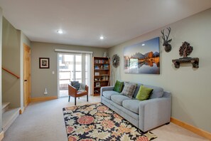 A living room with a grey sofa, a patterned rug, a bookshelf, and a door leading to a balcony. - Walk to Lake! Spacious Tahoe Retreat w/ Yard (South Lake Tahoe)