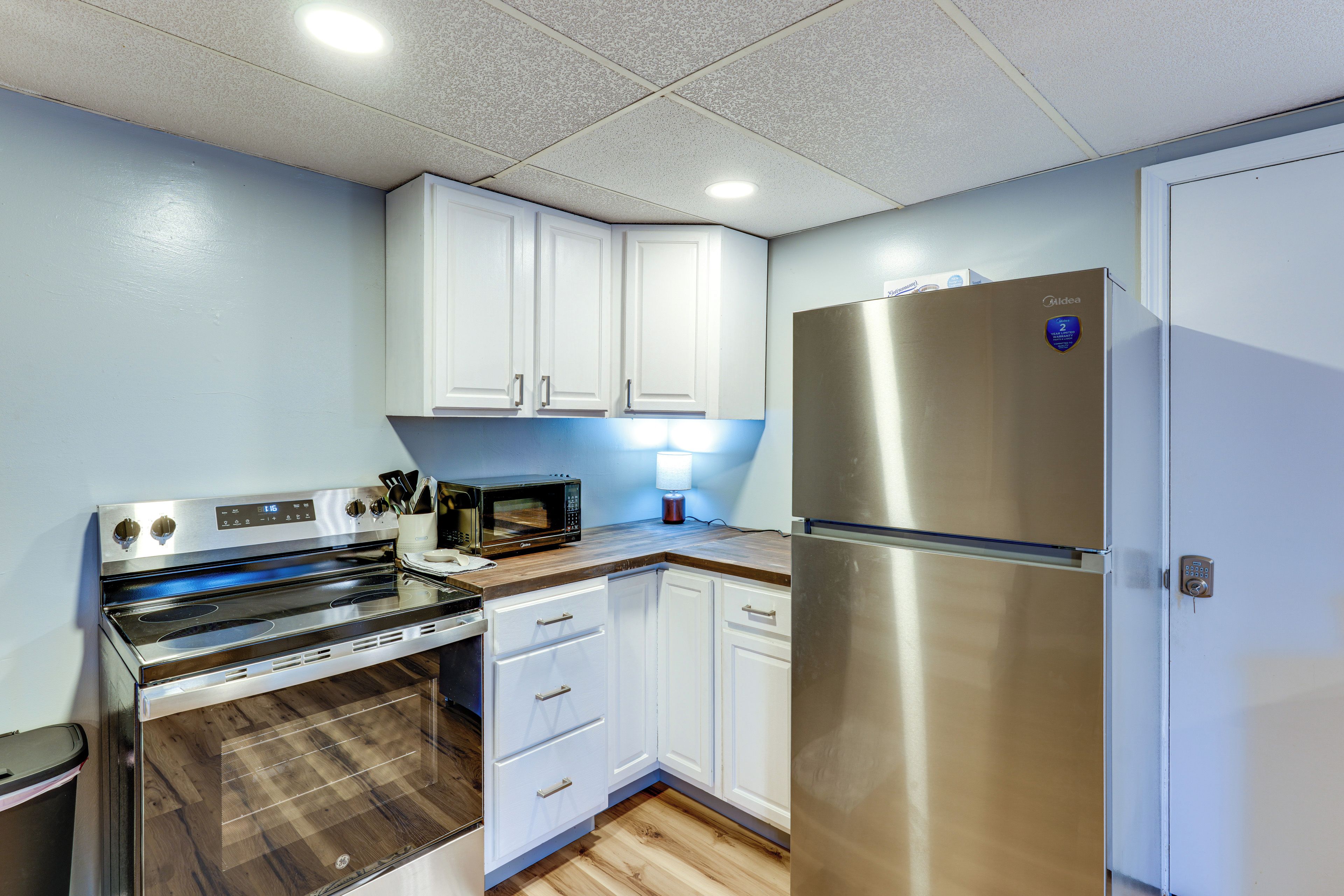 A compact kitchen with white cabinets, a stainless steel refrigerator, a microwave, and an oven.