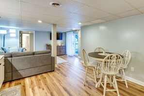 Ein geräumiger Wohnbereich mit grauem Sofa, Esstisch aus Holz mit weißen Stühlen und einem an der Wand befestigten Flachbildfernseher.
