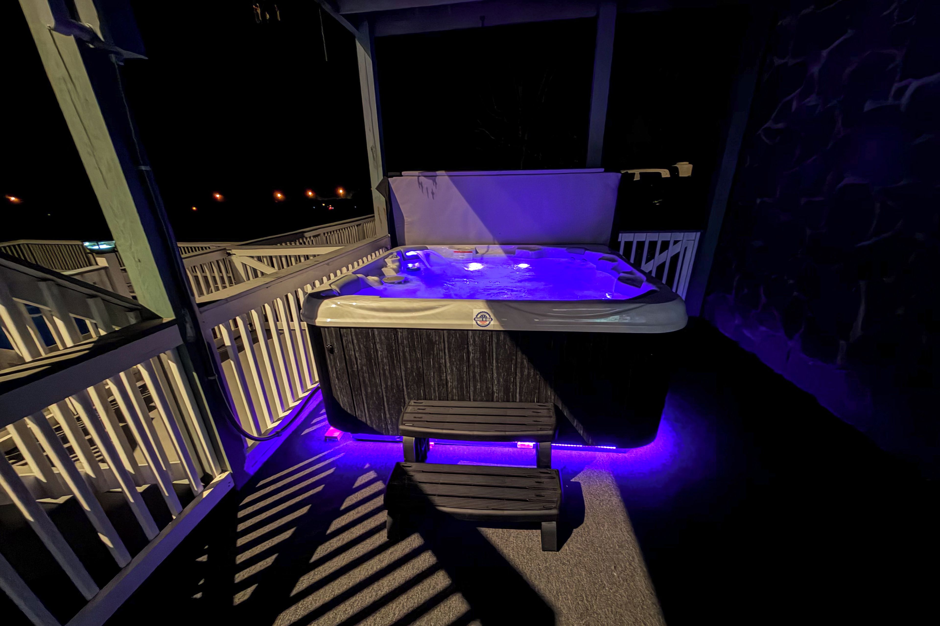 Un jacuzzi con revestimiento de madera e iluminación LED azul, ubicado en un balcón con barandilla.