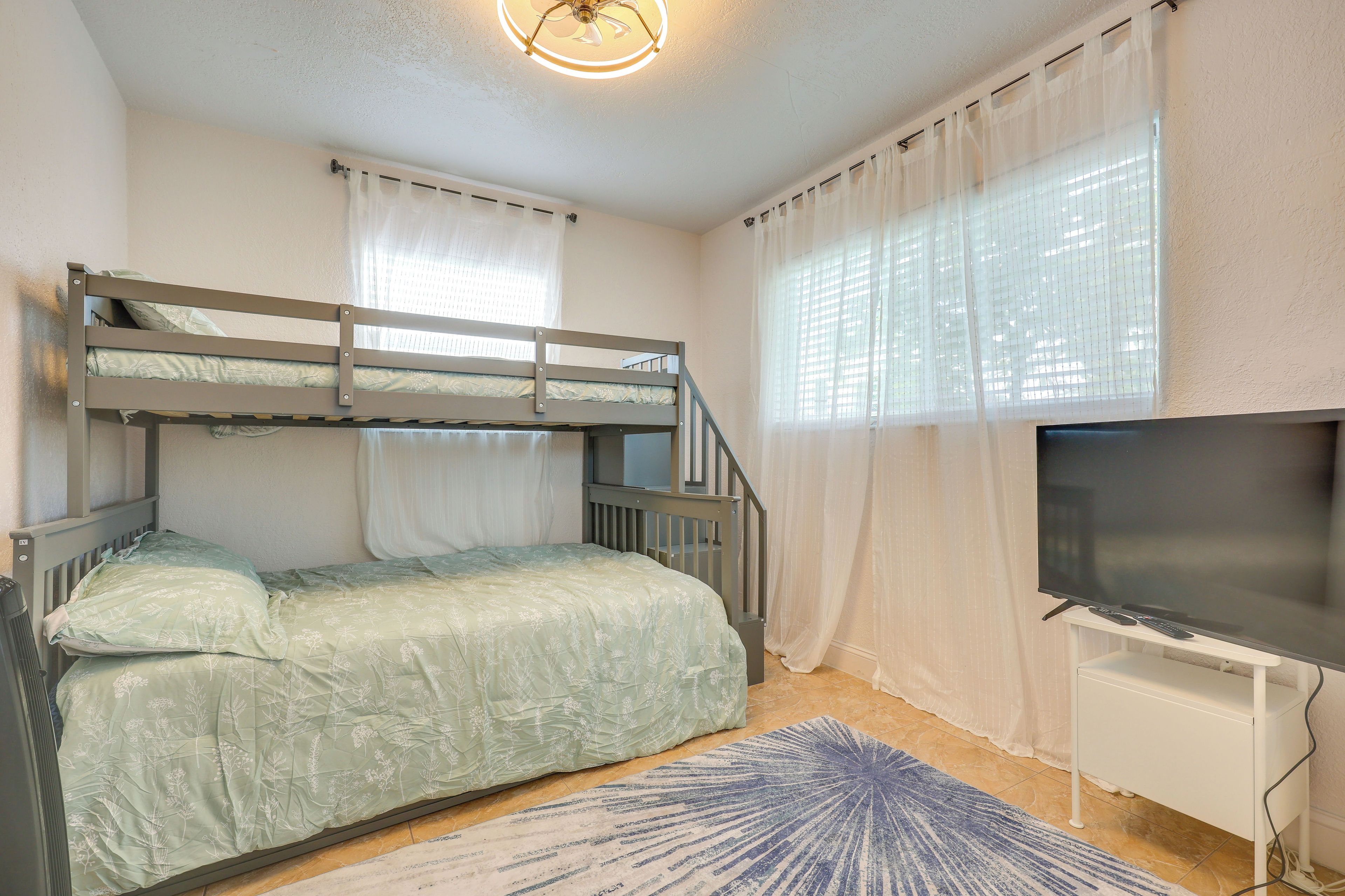 A room with bunk beds, a television, and a window with curtains.