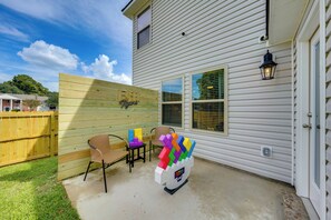 A residential exterior with a wooden fence, two chairs, a colorful toy structure, and a house with white siding and windows. - Walk to Tiger Stadium! New Modern Home w/ Yard (Baton Rouge)