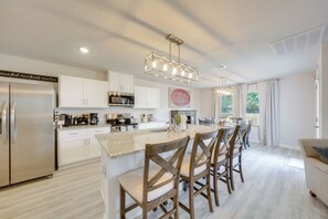 A modern kitchen with white cabinetry, stainless steel appliances, and a central island with bar stools. - Walk to Tiger Stadium! New Modern Home w/ Yard (Baton Rouge)