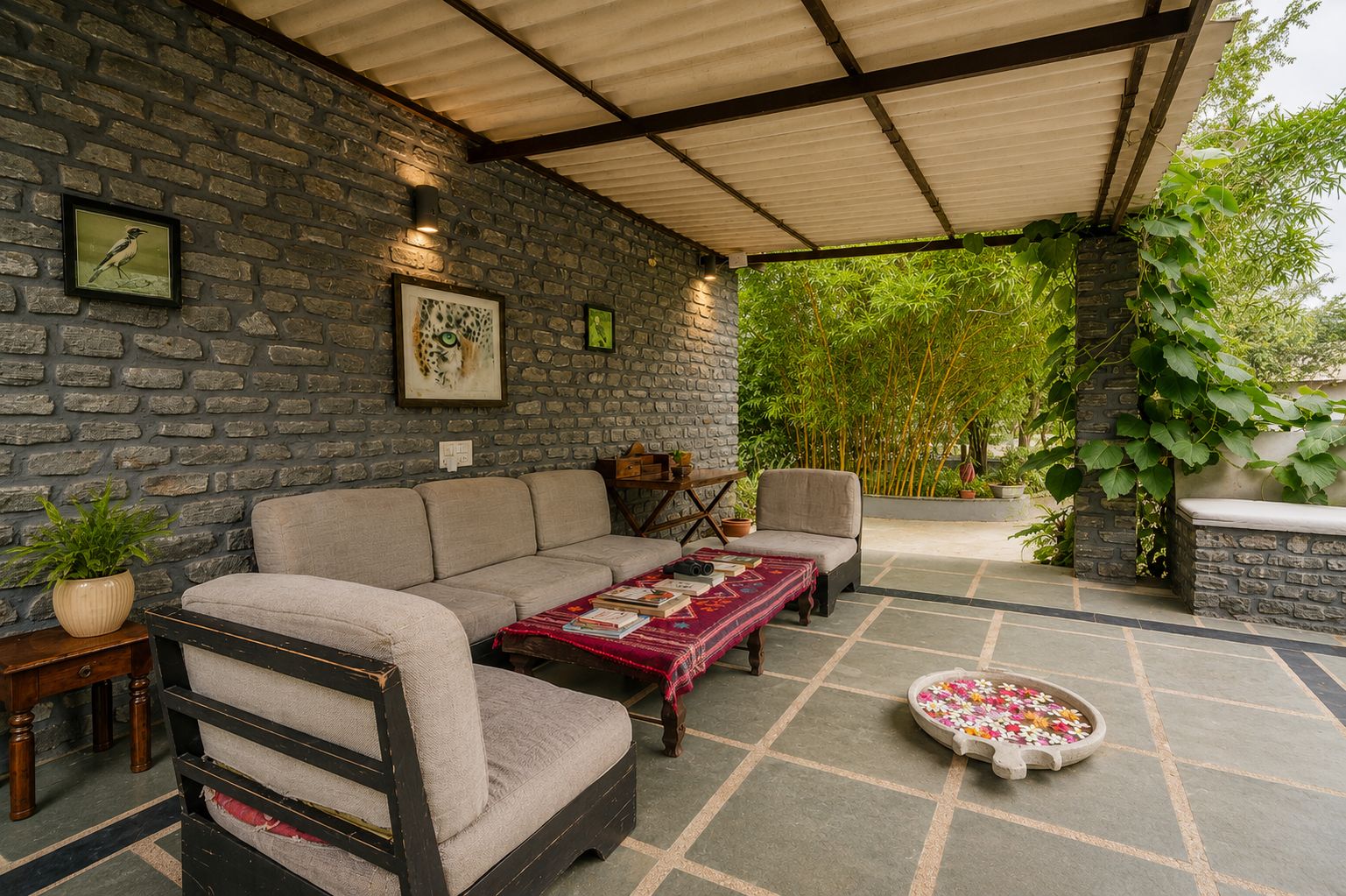 A covered outdoor seating area with a stone wall, a sofa, a coffee table, and a small table with a plant.