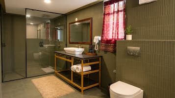 A modern bathroom with a glass shower enclosure, a wooden vanity with a white sink, a toilet, and a red patterned curtain.
