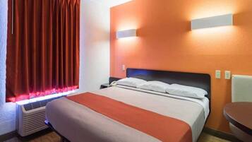 Ein Hotelzimmer mit einem Bett, einem Nachttisch, einem Sessel, einem Heizkörper und einem Vorhangfenster.