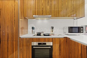 Een moderne keuken met houten kastjes, een Bosch inductiekookplaat, een Sharp magnetron en een inbouwoven.