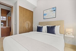 A modern hotel room with a large bed, a wooden wardrobe, a bedside table with a lamp, and a painting on the wall. - Niro by Kozystay - Kuningan (South Jakarta)