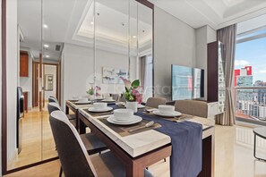A modern dining area with a long table set for four, a city view, and a flat-screen TV on the wall. - Niro by Kozystay - Kuningan (South Jakarta)