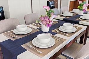 A dining table set with white plates, bowls, and cutlery, with a vase of flowers in the center. - Niro by Kozystay - Kuningan (South Jakarta)
