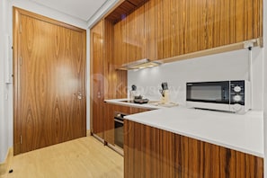 A modern kitchen with wooden cabinetry, a microwave, and a built-in oven. - Niro by Kozystay - Kuningan (South Jakarta)
