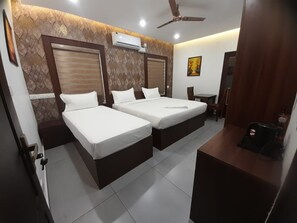 A hotel room with two beds, a ceiling fan, an air conditioning unit, and a small table with a kettle.