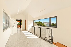 A modern interior with a hallway leading to a balcony, featuring a view of buildings and greenery. - The RED Signature 5br sunset (Đà Nẵng)