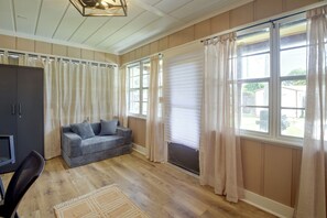 A room with a sofa, a TV, a window with curtains, and wooden flooring. - 8 Mi to New Smyrna Beach! Home w/ Poolside Oasis (Edgewater)
