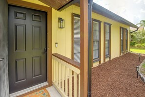 A house with a dark front door, a yellow exterior, and a wooden porch with a white railing. - 8 Mi to New Smyrna Beach! Home w/ Poolside Oasis (Edgewater)