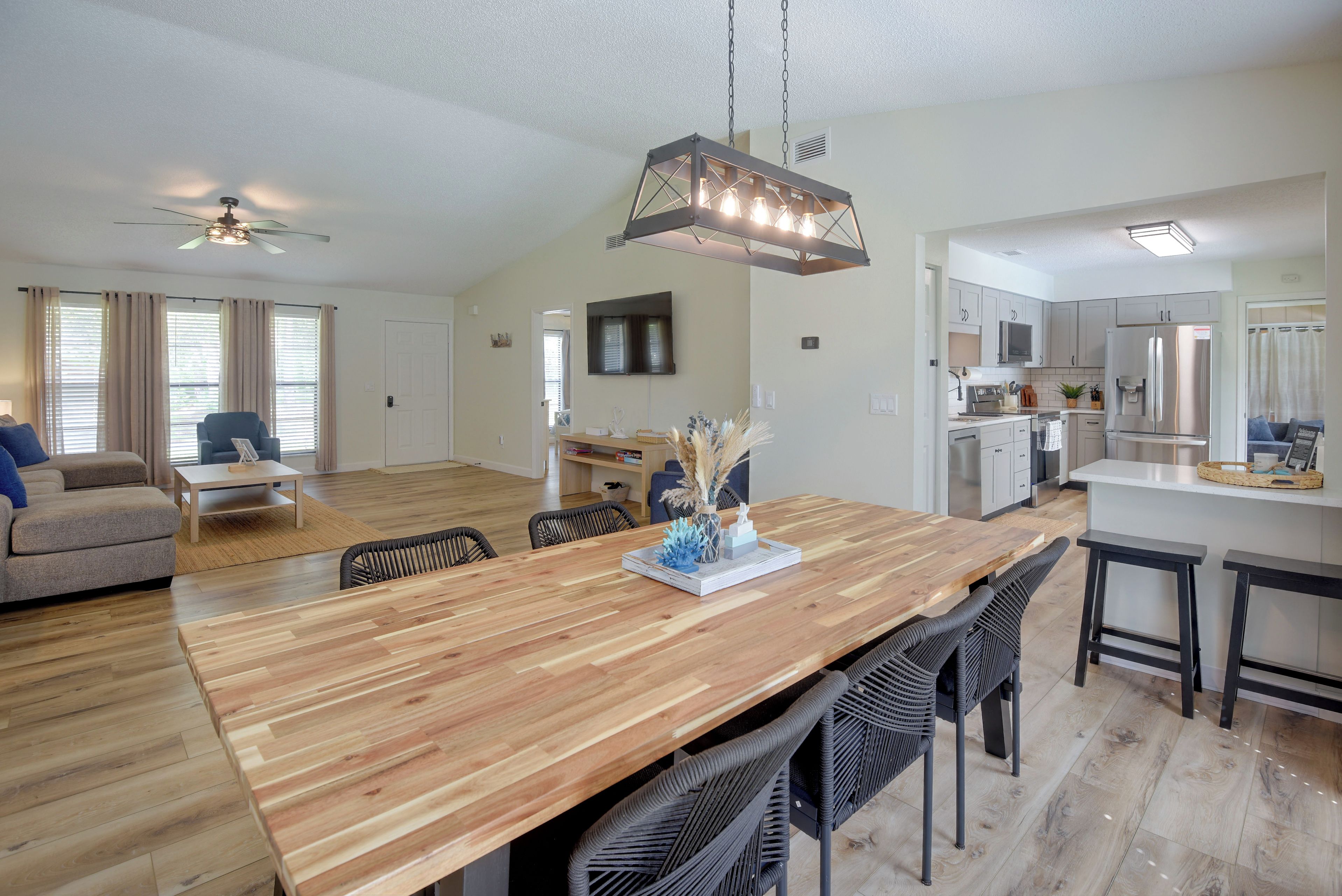 A modern kitchen with a central island, a dining area with a wooden table and chairs, and a living room with a sofa and a TV.
