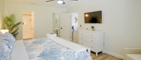 A bedroom with a bed, a ceiling fan, a TV, a dresser, and a plant.