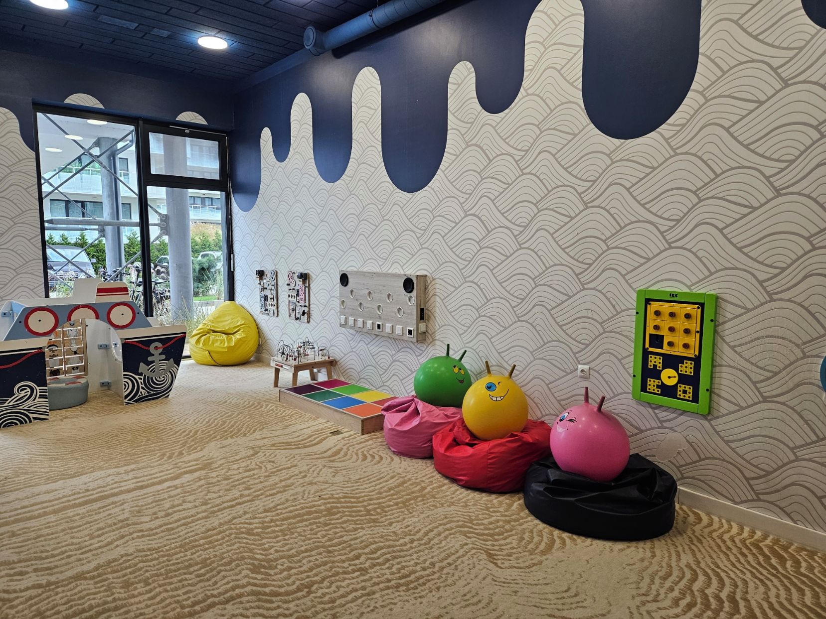 A room with a wave-patterned wall, a window, and a colorful bean bag area.