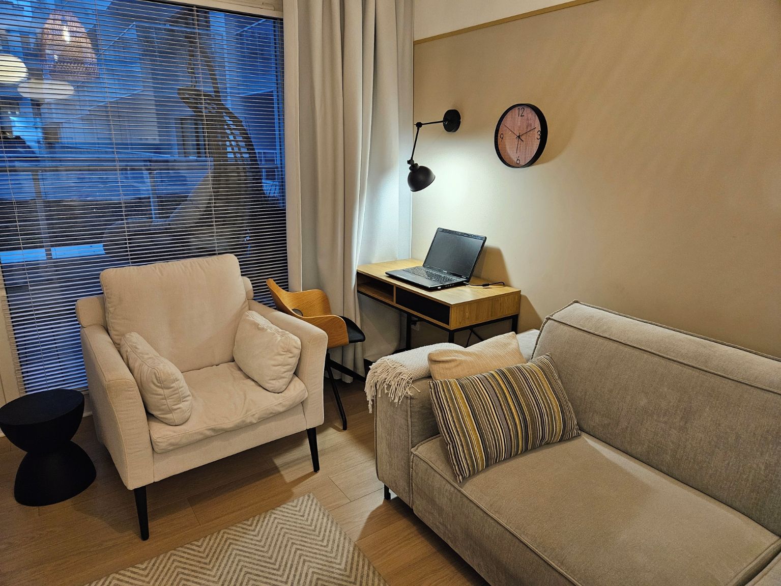A modern living room with a sofa, armchair, and a desk with a laptop.