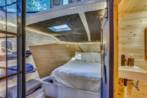 A compact, modern room with a bunk bed, a small seating area, and a wooden ceiling.