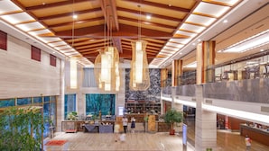 A spacious lobby with a high ceiling, modern chandeliers, and a large window with a view of trees. - Donghai Forest Hot Spring Hotel (Lianyungang)