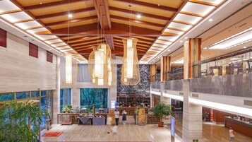 A spacious lobby with a high ceiling, modern chandeliers, and a large window with a view of trees.