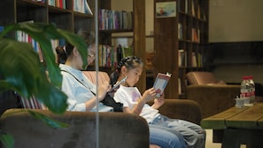 A library setting with bookshelves, a couch, and a table with a bottle.