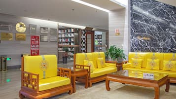 A lobby with yellow sofas and chairs, a glass coffee table, and a marble wall.