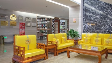 A lobby with yellow sofas and chairs, a glass coffee table, and a marble wall.