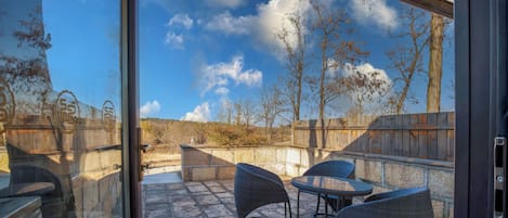 Un patio con piso de piedra, mobiliario de mimbre y vistas a un paisaje natural a través de un ventanal.