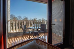 A balcony with a glass door, wicker furniture, and a view of trees.
