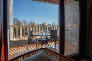 A balcony with a glass door, wicker furniture, and a view of trees.