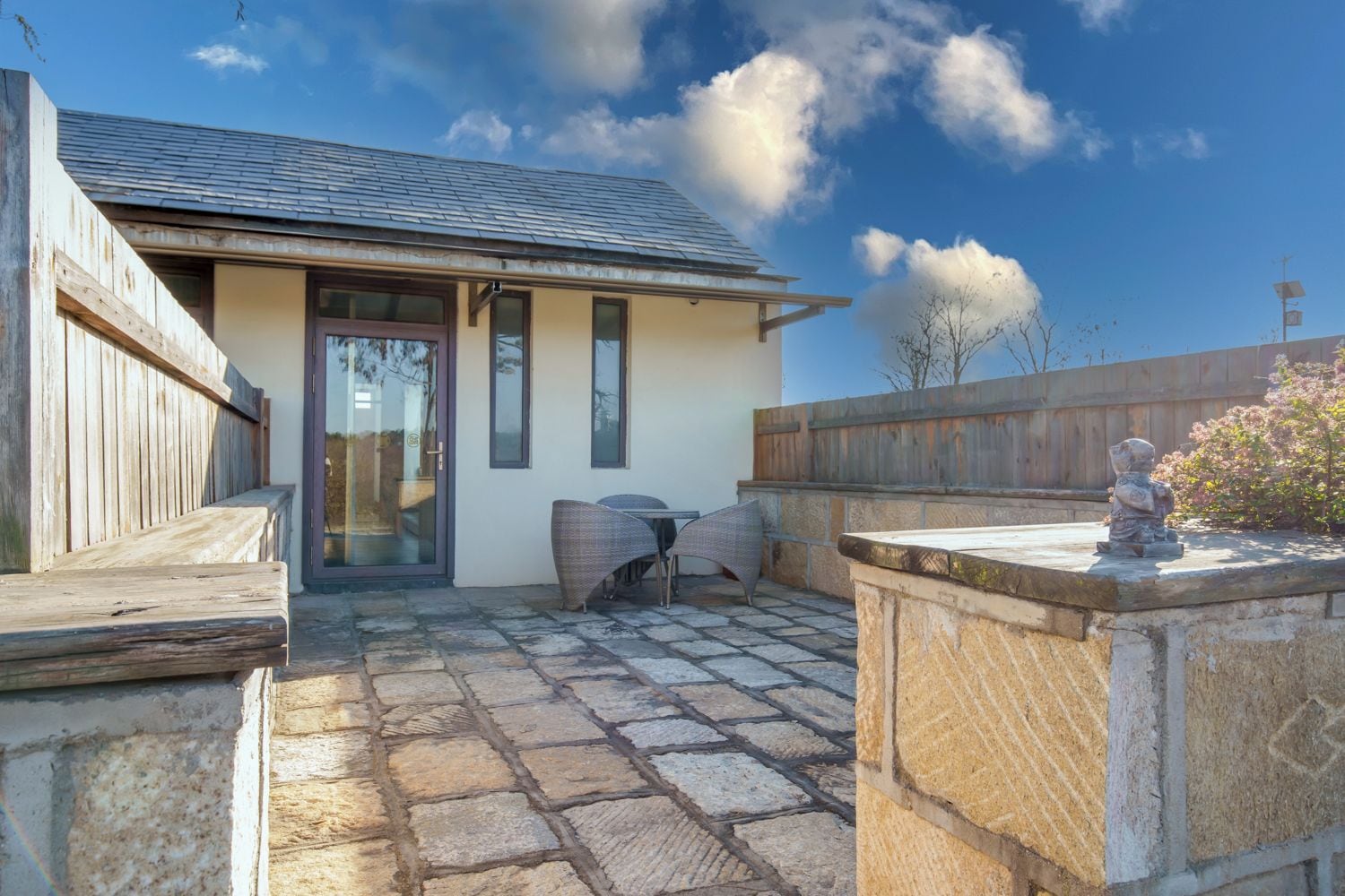 A building with a stone patio, a wooden fence, and a statue.