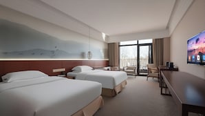 A hotel room with two beds, a desk, a chair, a TV, and a balcony with a view. - Donghai Forest Hot Spring Hotel (Lianyungang)