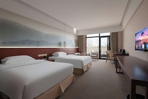 Quarto de hotel com duas camas, uma escrivaninha, uma cadeira, televisão e varanda com vista.