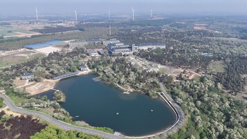 Vista aérea de un campus con un lago, edificios y aerogeneradores al fondo.